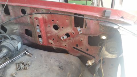 1985 Ford Bronco - The firewall of a vehicle's engine bay shows exposed metal and wiring, with tools nearby.