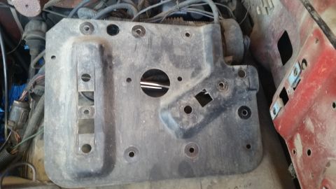 1985 Ford Bronco - A gray metal bracket with various holes and cutouts is visible in an engine bay, adjacent to a red painted component.