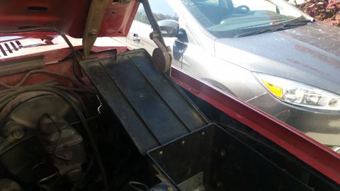 1985 Ford Bronco - The underhood toolbox is visible in the engine bay of a red vehicle, with a silver car parked behind it.