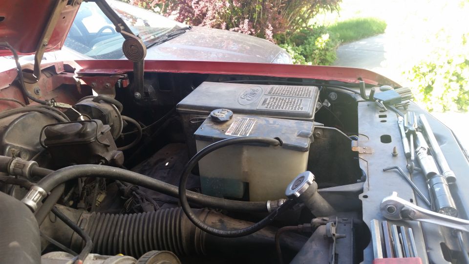 Engine bay with coolant reservoir and fuse box visible. Tools are laid out on the fender