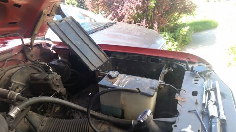 1985 Ford Bronco - The engine bay of a red vehicle is shown with the hood open, revealing various components and a toolbox.