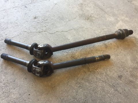 1984 Ford Bronco - Close-up view of two automotive drive shafts resting on a textured concrete floor.