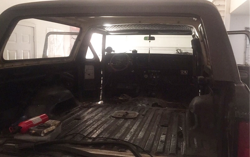 Interior of a classic Ford Bronco, rear view looking forward. Empty cargo area, ribbed floor, dashboard, steering wheel.
