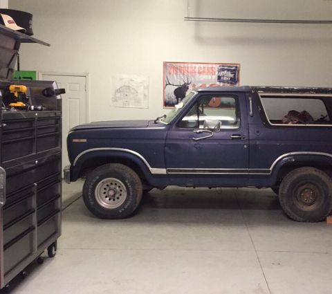 1979 Ford Bronco - A dark blue Ford Bronco is parked inside a garage next to a tool chest. A poster of an elk and beer cans hangs on the wall behind the vehic…