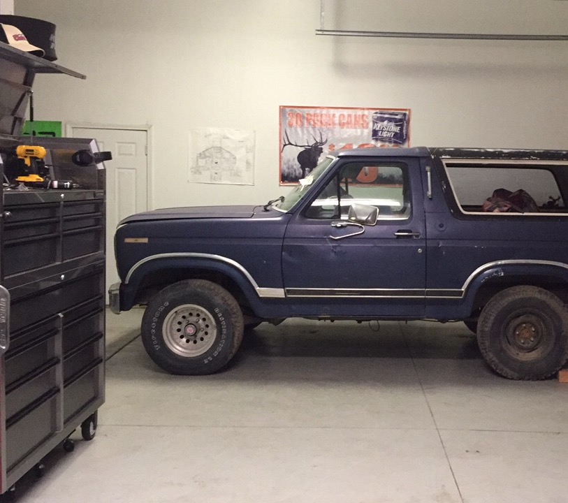 Dark blue Ford Bronco parked in a garage with a tool chest and a poster on the wall.