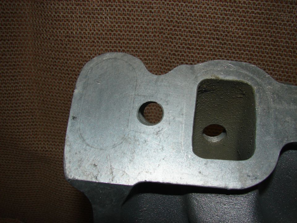 Cast metal intake manifold with rectangular and circular ports.