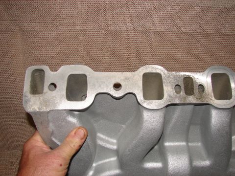 1973 Ford Ranchero - A hand holds a gray aluminum intake manifold with four ports visible on the top surface. The manifold has a silver metal gasket surface wit…