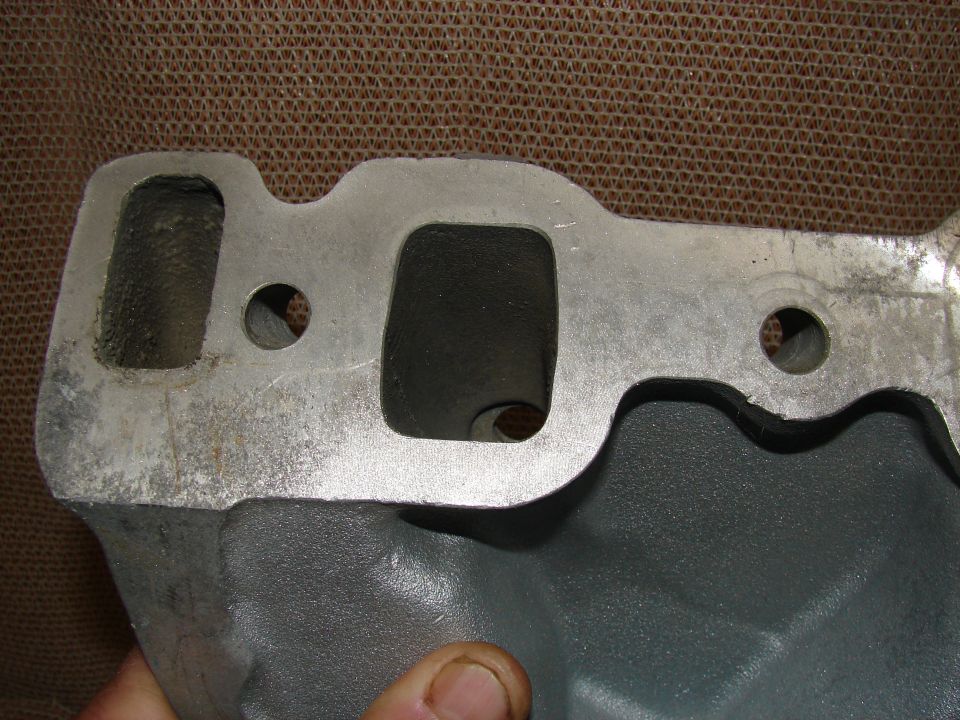Cast aluminum intake manifold with two ports, dark gray and silver finish, textured brown background.