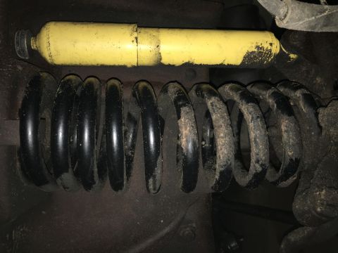 1980 Ford Bronco - A yellow shock absorber is visible above a black coil spring. Both parts appear to be from the suspension system of a vehicle, and show sig…