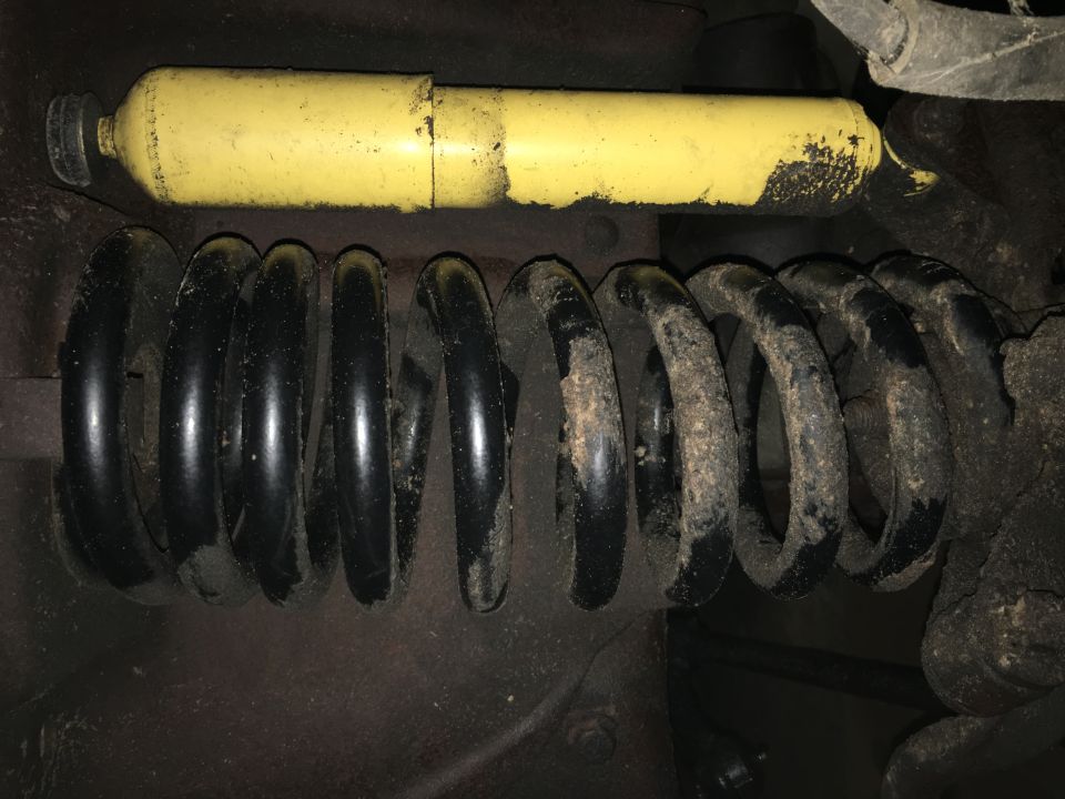 Yellow shock absorber above a black coil spring, likely from a vehicle suspension.