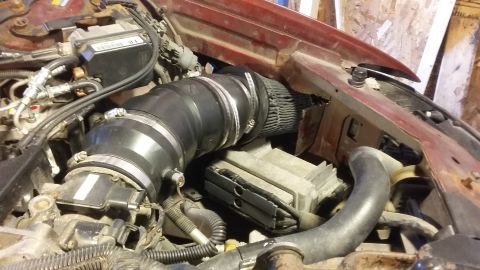 2000 Pontiac Grand Prix - The image shows a close-up view of the engine bay of a red vehicle, focusing on the intake system. A large black intake tube with metal cla…