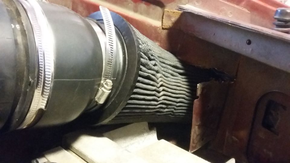Black air intake hose connected to a pleated gray air filter in a red engine bay.