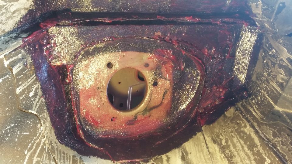Vehicle undercarriage component covered in red grease with a central opening.