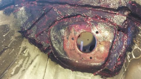 2000 Pontiac Grand Prix - A close-up view of a car's chassis showing a circular metal component with three holes, coated in a thick, dark purple substance. The surro…