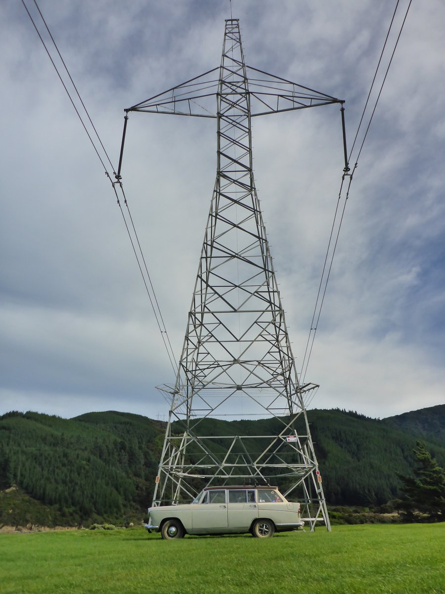 Light-colored station wagon parked under a large electricity pylon.
