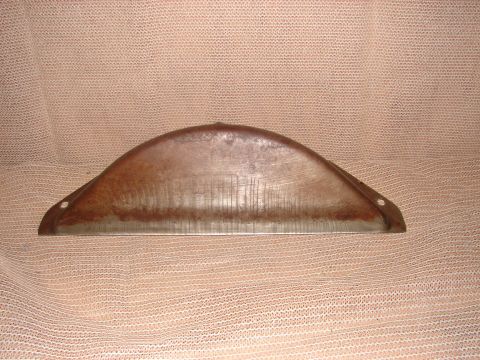 1973 Ford Ranchero - A curved, metallic part with a rusty patina and visible horizontal striations is shown against a textured, light brown background. The part…