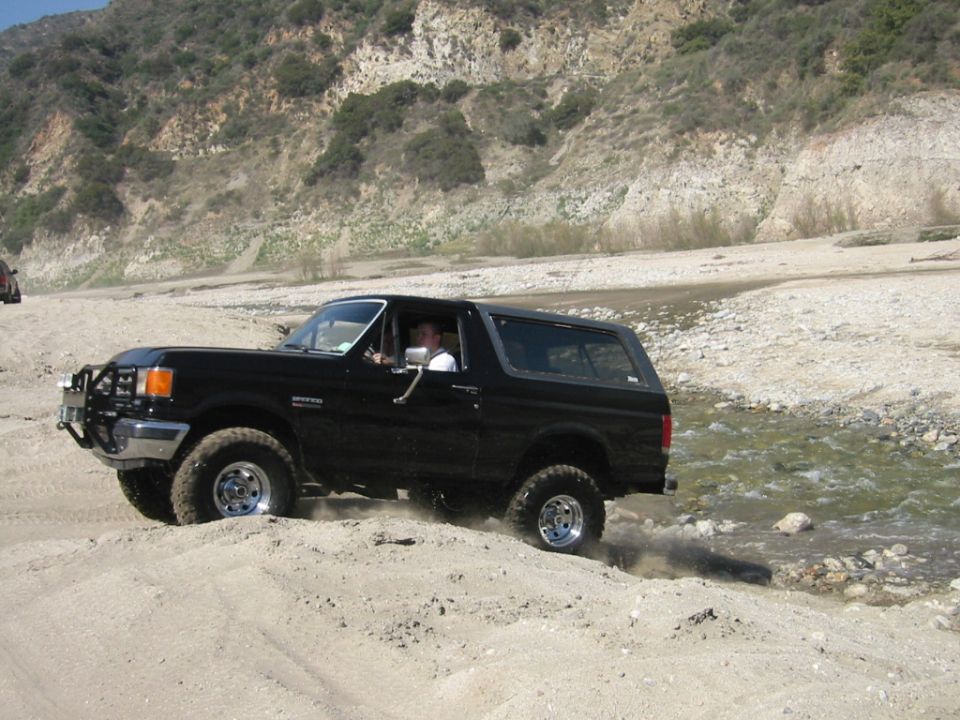 Black Ford Bronco SUV driving over sand in a rocky canyon riverbed