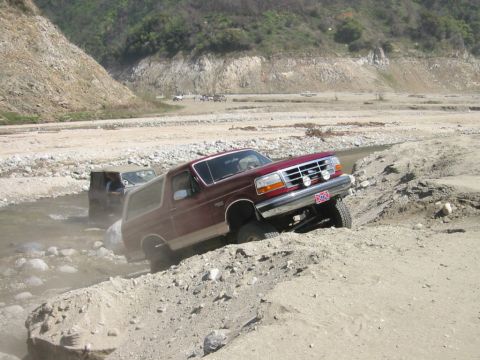 1985 Ford Bronco - This maroon Ford Bronco appears to be from the early to mid-1990s, not 1985, as it navigates a challenging off-road terrain.