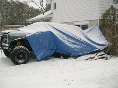 1986 Ford Bronco - A partially covered SUV sits in the snow, its tires and front fender visible.