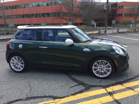 2001 Ford Crown Victoria - A dark green Mini Cooper is parked in a cracked asphalt parking lot in front of a modern orange building. The car is viewed from the side,…