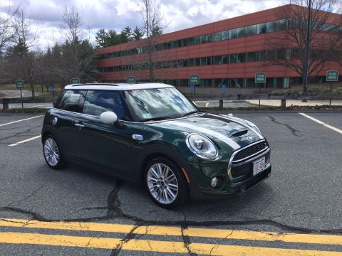 2001 Ford Crown Victoria - A dark green Mini Cooper S is parked in a parking lot in front of a modern office building. The car has white racing stripes on the hood an…