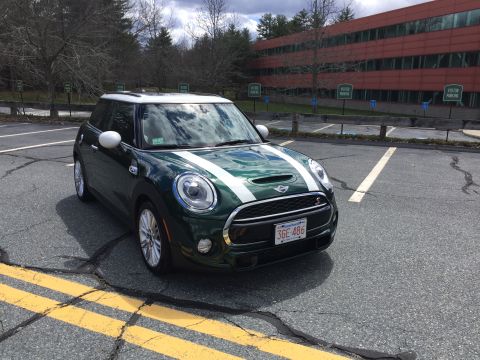 2001 Ford Crown Victoria - A dark green Mini Cooper S is parked in a parking lot with yellow lines and a modern building in the background. The car has white racing s…