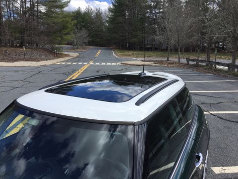 2001 Ford Crown Victoria - The top of a white and dark green Mini Cooper is shown parked on an asphalt road with trees in the background. The car has a sunroof and ro…
