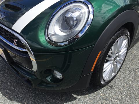 2001 Ford Crown Victoria - Close-up front view of a dark green Mini Cooper with white racing stripes on the hood. The vehicle features a chrome grille, a large headli…
