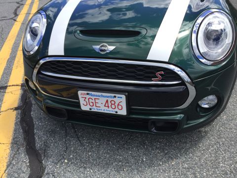 2001 Ford Crown Victoria - A close-up, low-angle shot of the front grille and headlights of a dark green Mini Cooper S. The car has white racing stripes on the hood a…