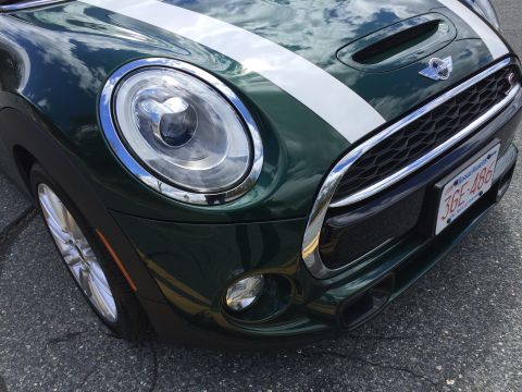 2001 Ford Crown Victoria - Close-up front view of a dark green Mini Cooper with white racing stripes. The vehicle is parked on asphalt with yellow road markings visib…