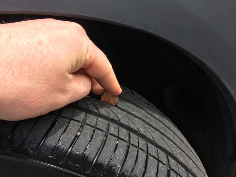 2001 Ford Crown Victoria - A hand holds a penny against the tread of a car tire, indicating tire wear. The tire appears to be on a sedan or similar vehicle.