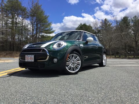 2001 Ford Crown Victoria - A dark green Mini Cooper S is parked on an asphalt road with yellow lane markings. The car has white racing stripes on the hood and a white…