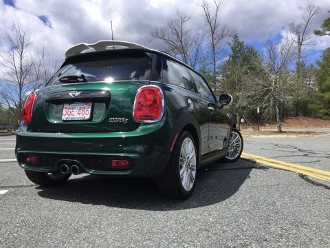 2001 Ford Crown Victoria - The rear driver's side quarter view of a dark green Mini Cooper S hatchback is shown parked on an asphalt road with yellow double lines. Th…