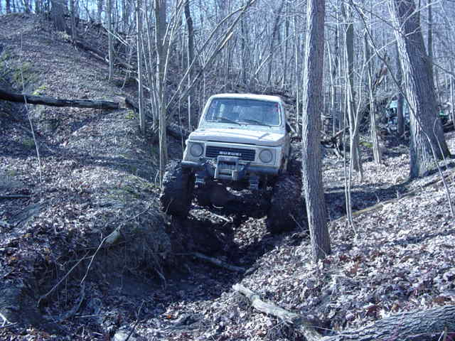 White Suzuki Samurai climbing a muddy hill in a forest