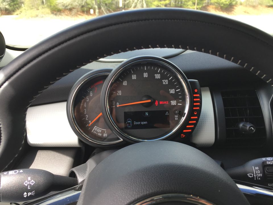Close-up of car interior with steering wheel and instrument cluster, showing a "Door open" warning.