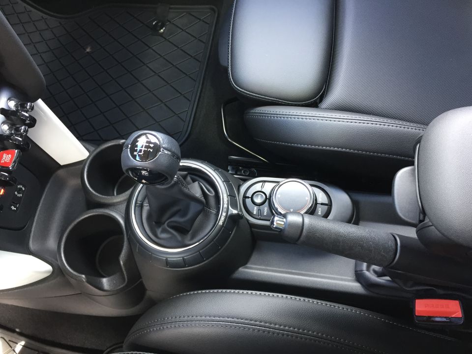 Close-up of a manual shift knob with gear pattern, center console, and cup holders in a car.