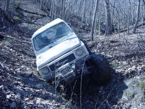 1992 Ford Bronco - Suzuki Samurai navigating a steep, wooded trail, showing its grille.