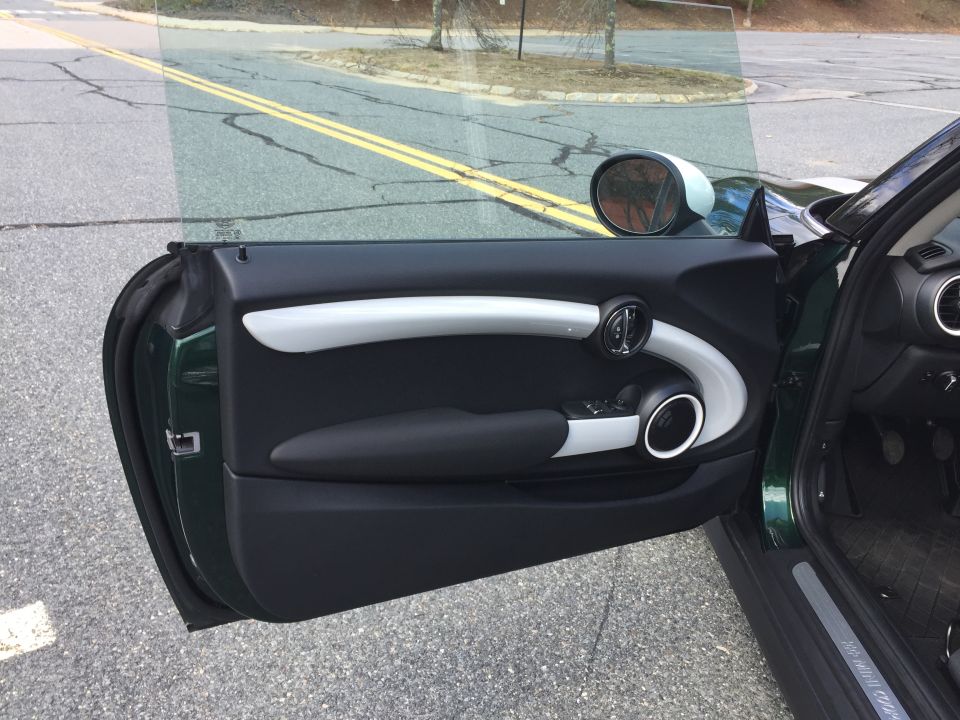 Open driver's side door of a dark green Mini Cooper, showing interior door panel and exterior.
