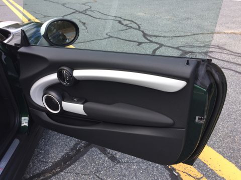 2001 Ford Crown Victoria - The interior door panel of a dark green Mini Cooper is shown, featuring a silver and black door handle and armrest. The car door is open, r…