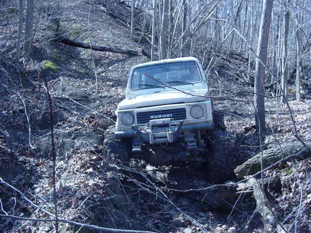 Suzuki Samurai climbing a muddy, wooded hill with a winch on the front