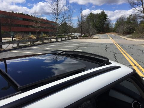 2001 Ford Crown Victoria - The image shows the open sunroof and roofline of a white vehicle, reflecting a cloudy sky. In the background, there is a parking lot and a…