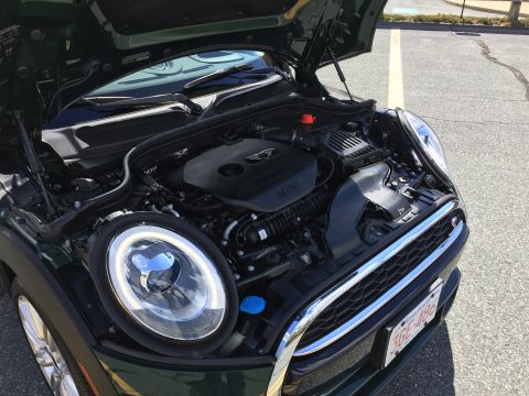 2001 Ford Crown Victoria - The engine bay of a dark green Mini Cooper is shown with the hood open. The front grille and headlight are visible.