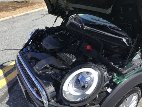 2001 Ford Crown Victoria - The open hood of a dark green Mini Cooper reveals its engine bay and the front headlight assembly. The vehicle is parked on an asphalt road…