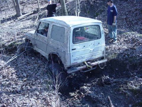1992 Ford Bronco - A white Suzuki SUV is stuck in the mud on a wooded trail.