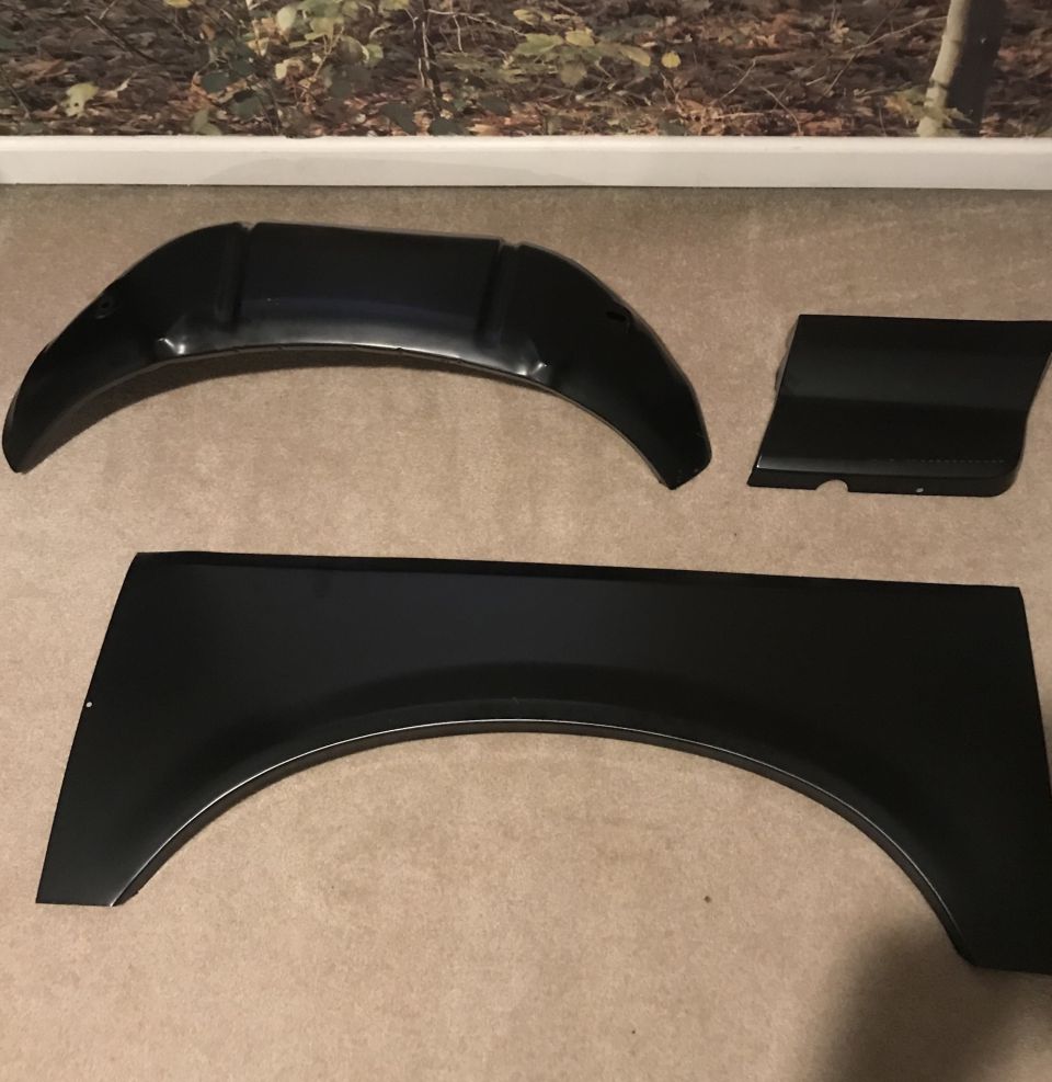 Three black automotive fender flare parts on a carpeted floor.
