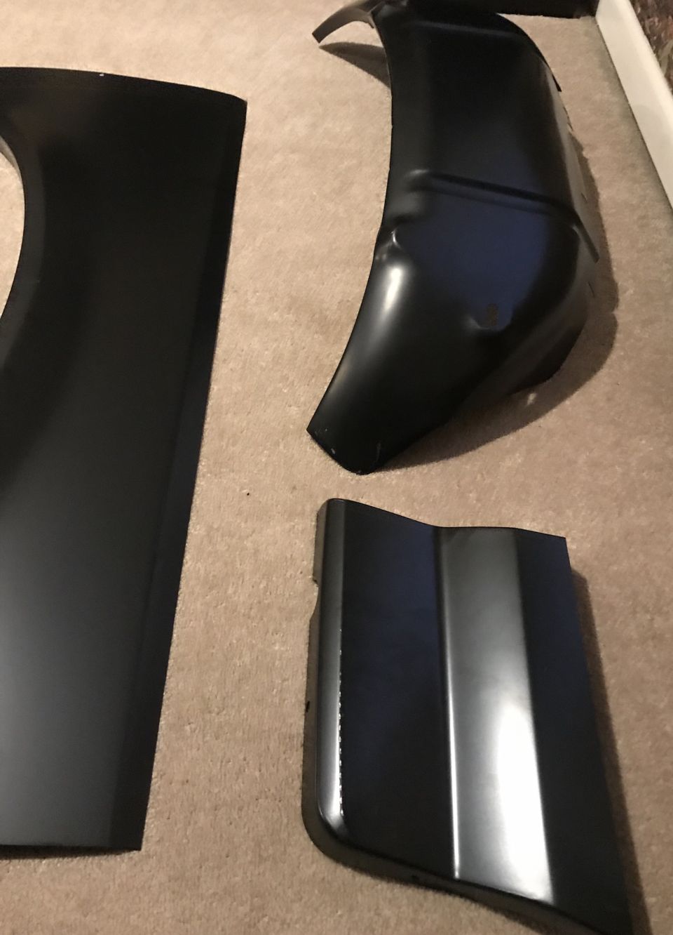 Three black metal car body panels on carpet
