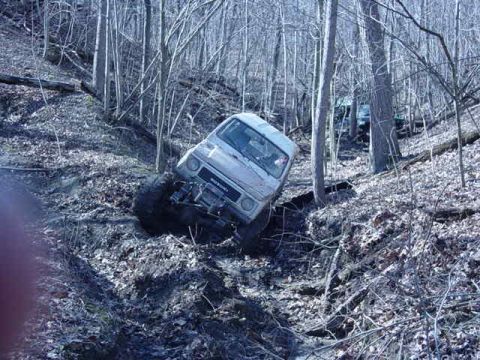 1992 Ford Bronco - An off-road vehicle navigates a challenging, muddy incline within a dense forest setting.