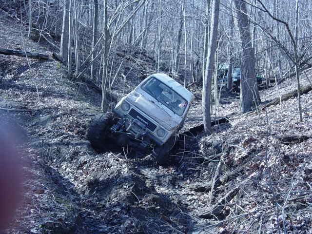 White off-road vehicle climbing a steep, muddy hill in a forest