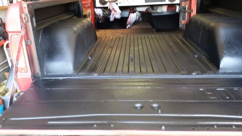 1968 Ford Bronco - The bed of a red pickup truck has been lined with a black protective coating. The tailgate is down, revealing the ribbed metal floor and wh…
