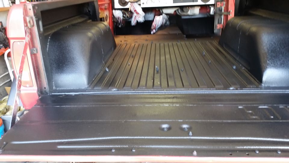 Black protective coating applied to the bed of a red pickup truck with the tailgate down.
